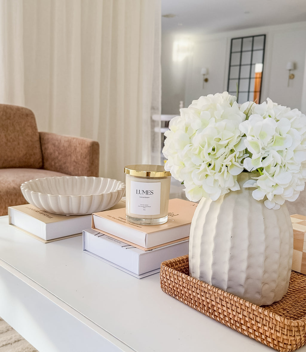 Decorative setup on a coffee table with a vase of white flowers, books, and a candle.