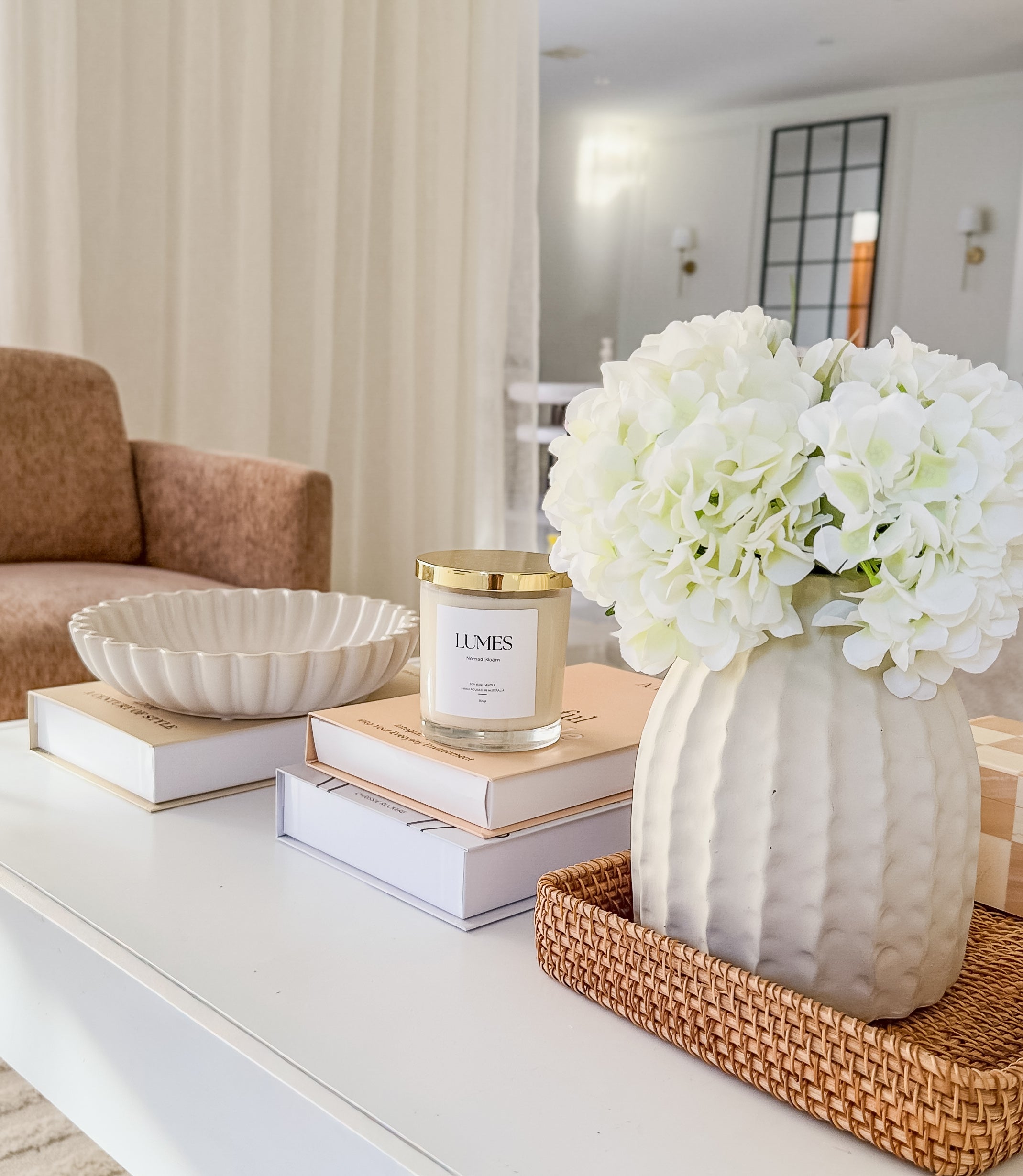 Decorative setup on a coffee table with a vase of white flowers, books, and a candle.