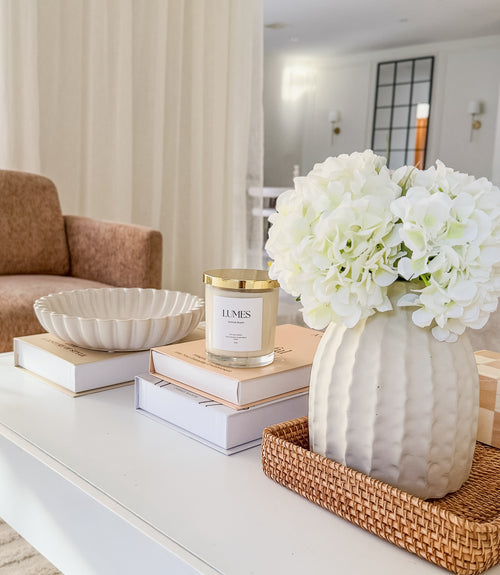 Decorative setup on a coffee table with a vase of white flowers, books, and a candle.